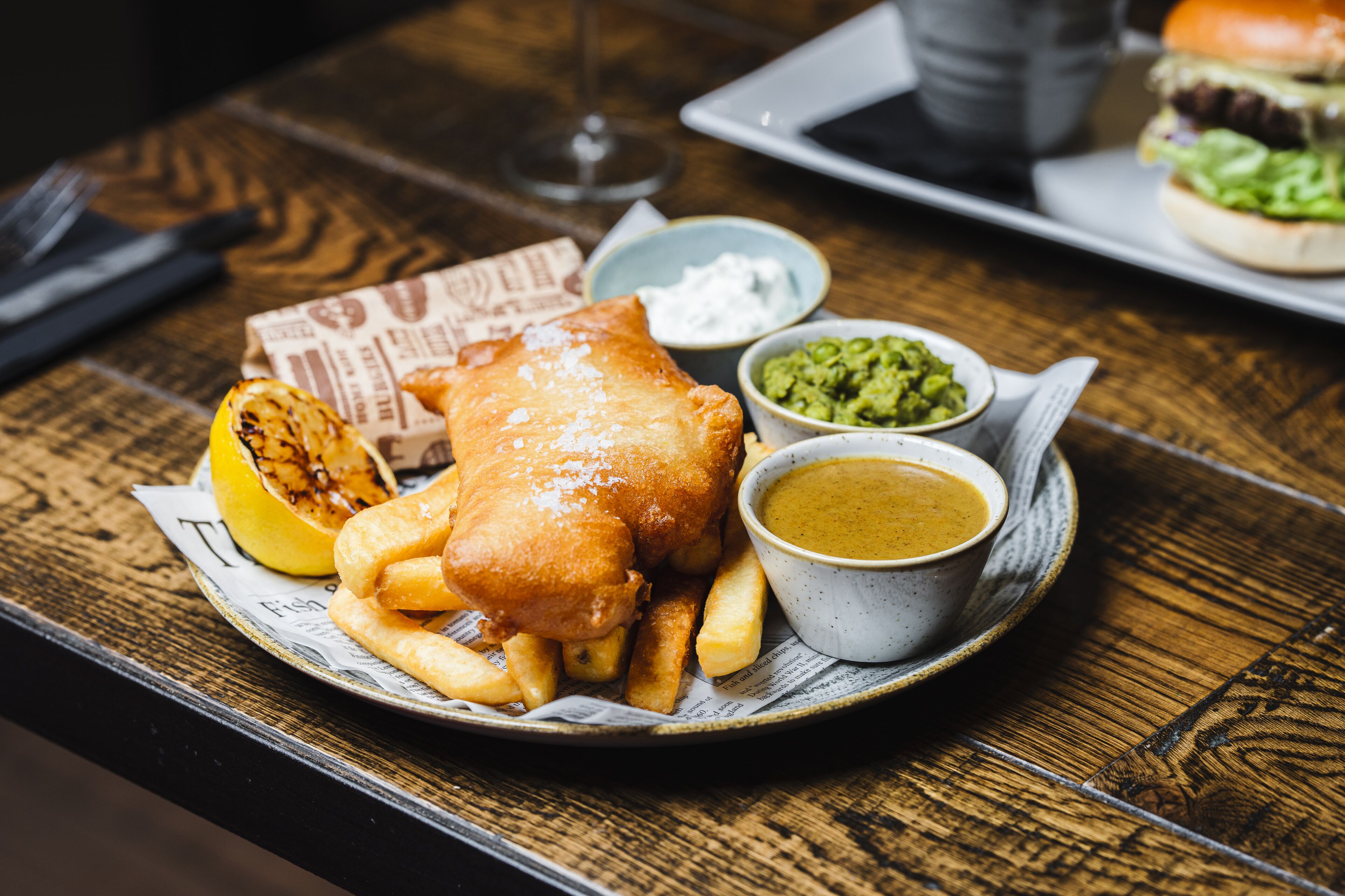 A plate of fish and chips with lemon, tartar sauce, and mushy peas on a wooden table.