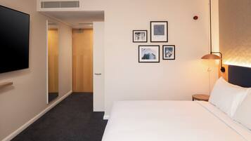 A hotel room with a bed, a TV, a wall-mounted heater, and framed pictures on the wall.