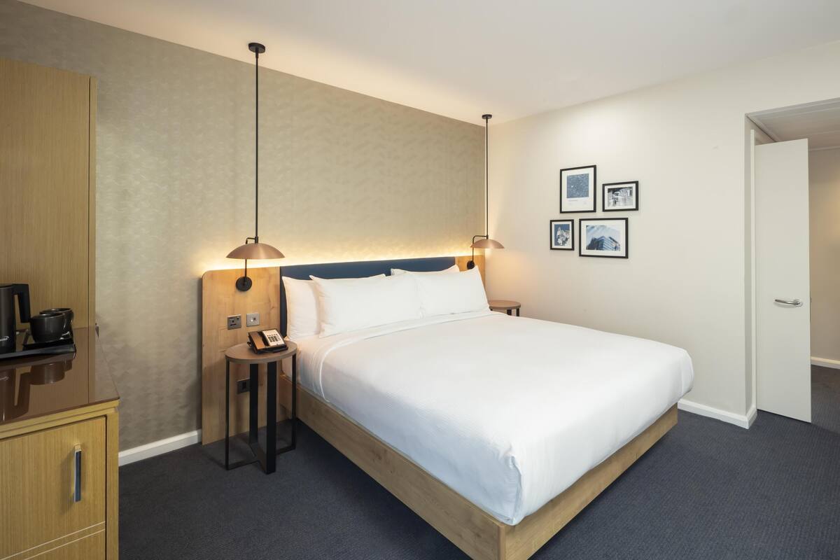 A hotel room with a single bed, bedside tables, a desk with a telephone, and a wardrobe.