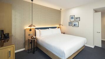 A hotel room with a single bed, bedside tables, a desk with a telephone, and a wardrobe.