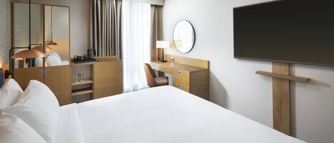 Habitación de hotel con una cama grande, un escritorio con silla, un espejo, un televisor de pantalla plana y una ventana con cortinas.
