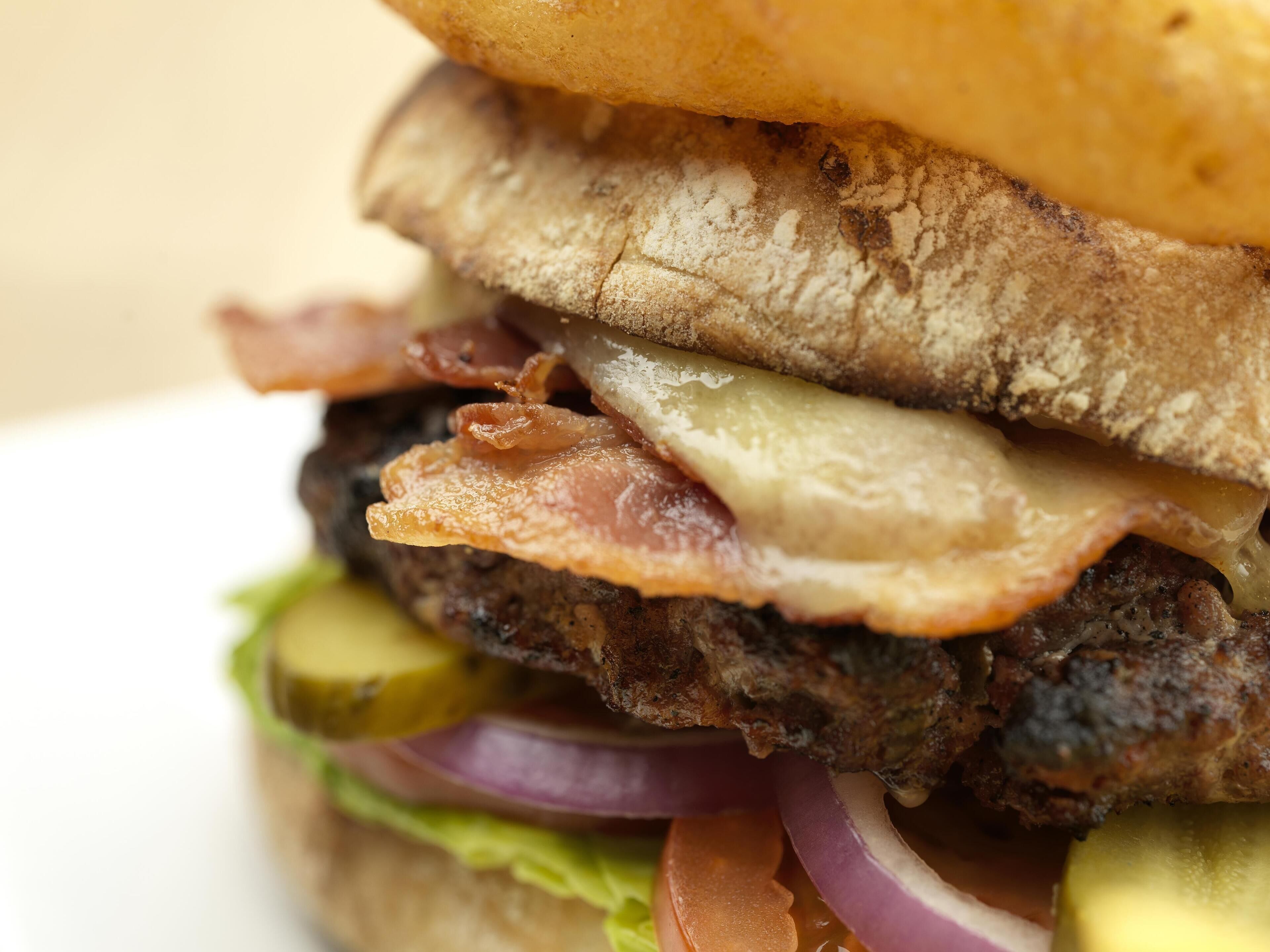 Primer plano de un sándwich con capas de tocino, queso y pepinillos.