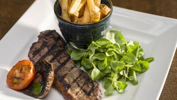 A plate with grilled steak, fries, a tomato, and greens.