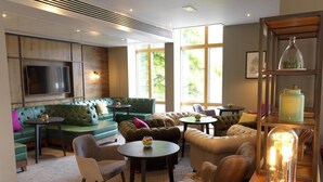 A modern lounge area with leather sofas, round tables, and a large flat-screen TV. - Hilton Garden Inn Birmingham Brindley Place (Birmingham)