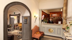 A reception area with a reception desk, a seating area with a bench, and a wall-mounted display case with various items. - Hotel Villa Glori (Rome)