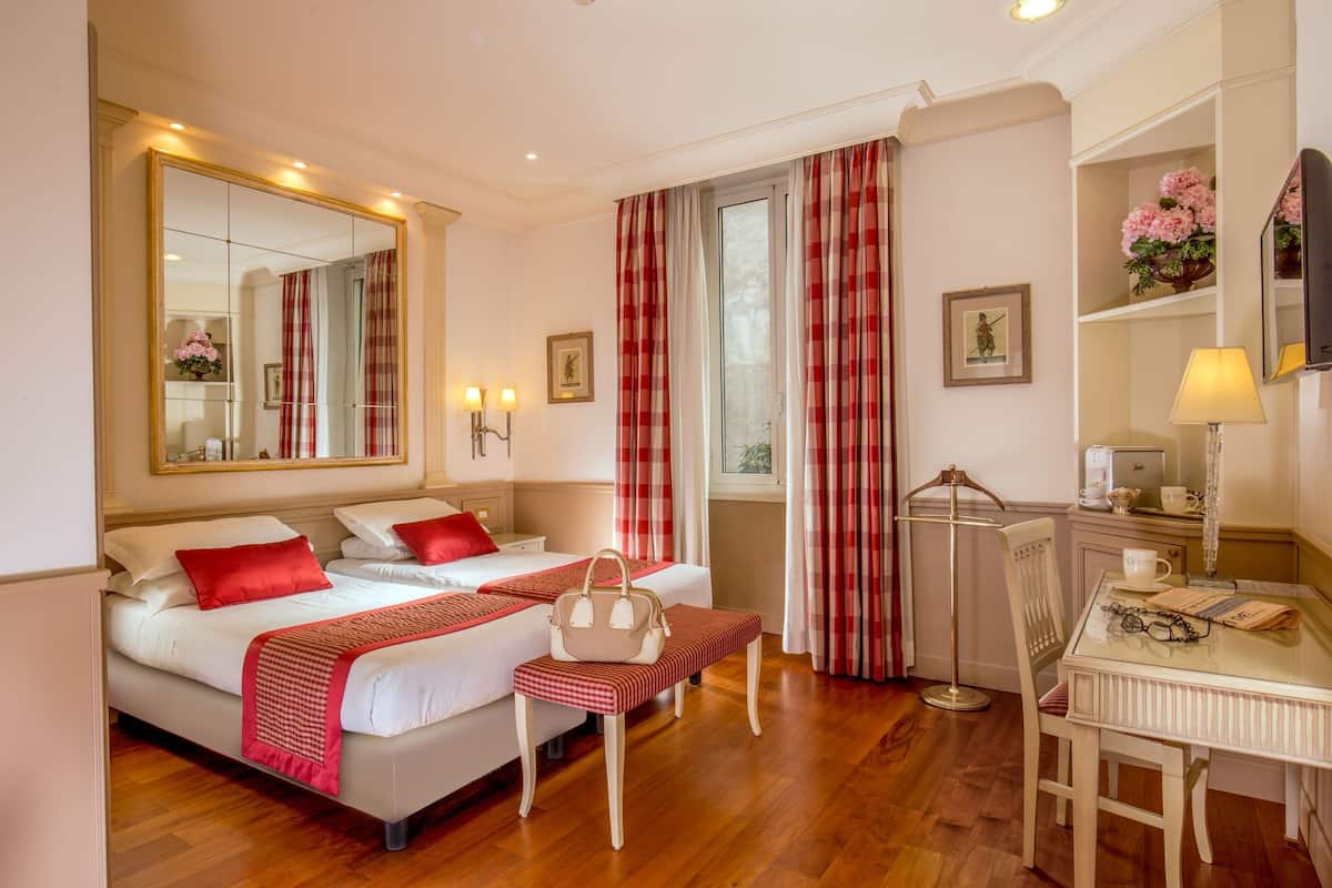 A hotel room with a large bed, a desk with a chair, a mirror, and a window with curtains.