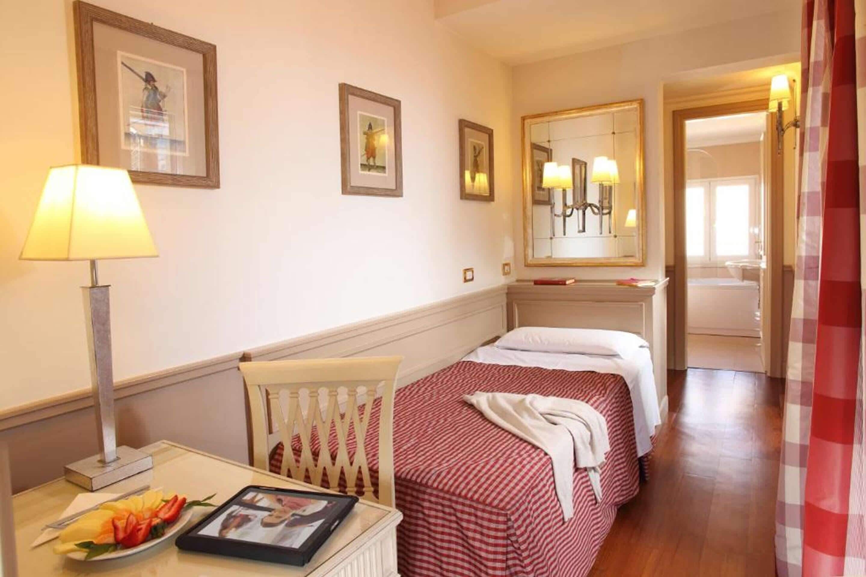 A hotel room with two beds, a bedside table with a lamp, a chair, and framed pictures on the wall.