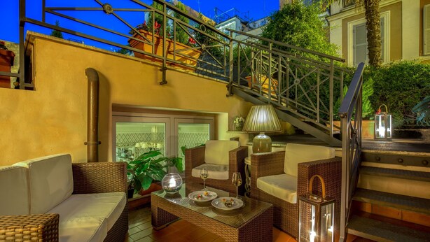 A cozy outdoor seating area with wicker furniture, a glass-top table, and a staircase leading to an upper level. - Hotel Villa Glori (Rome)