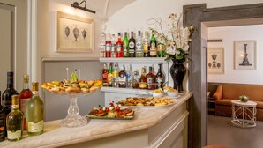 A bar area with a variety of bottles, a cake stand with pastries, and a seating area with a sofa and a small round table. - Hotel Villa Glori (Rome)