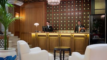 Zona de recepción de un hotel con un panel de madera que muestra los números de las habitaciones, una araña y un mostrador de recepción.