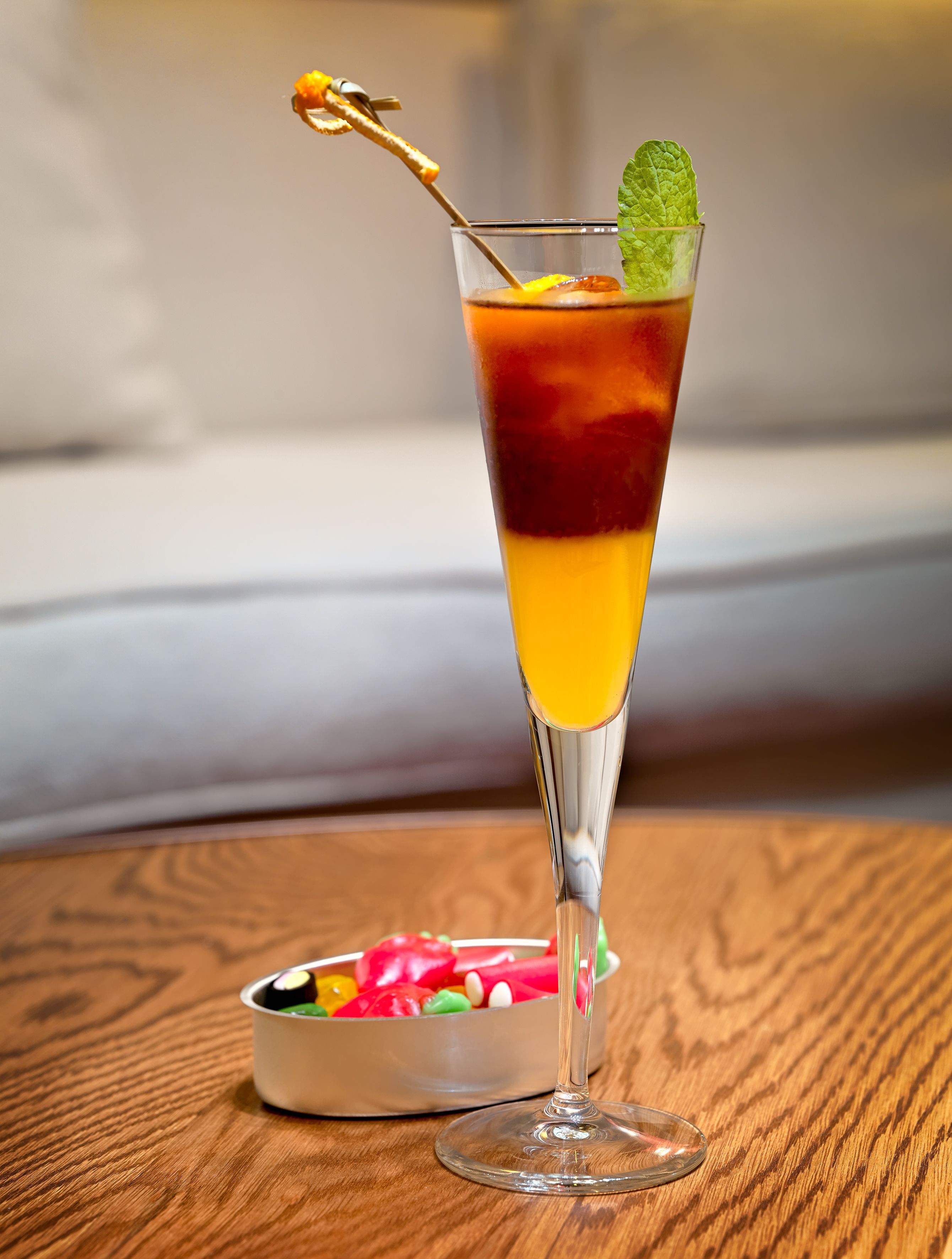 A cocktail glass with a layered drink, garnished with a mint leaf, on a wooden table.
