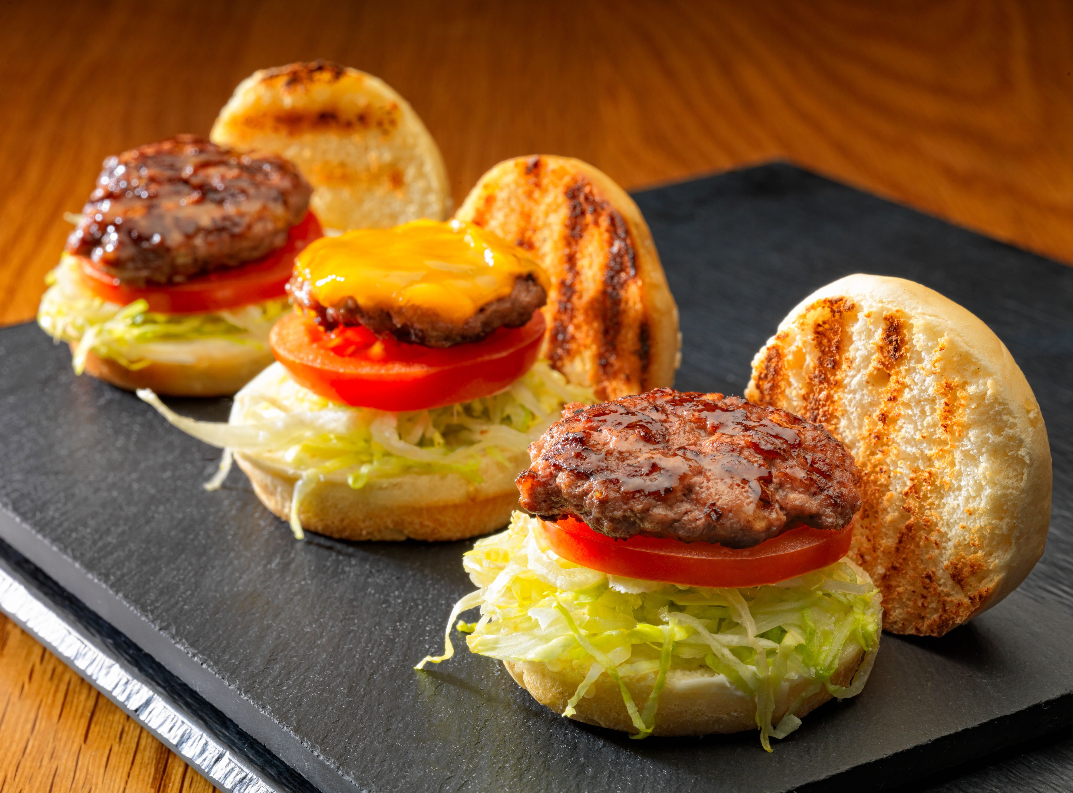 Een sandwich met een gegrilde burger, kaas, sla en tomaat op een geroosterde bol.