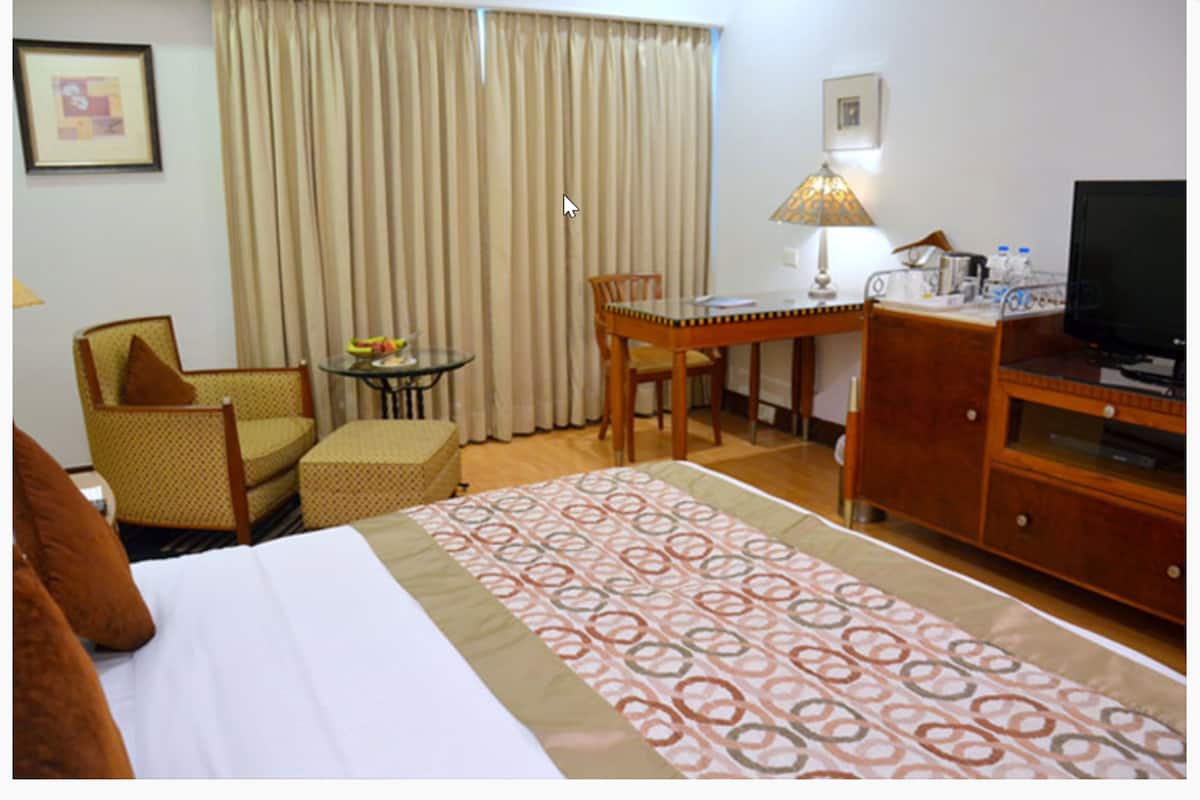 A hotel room with a bed, a desk, a chair, a television, and a lamp.