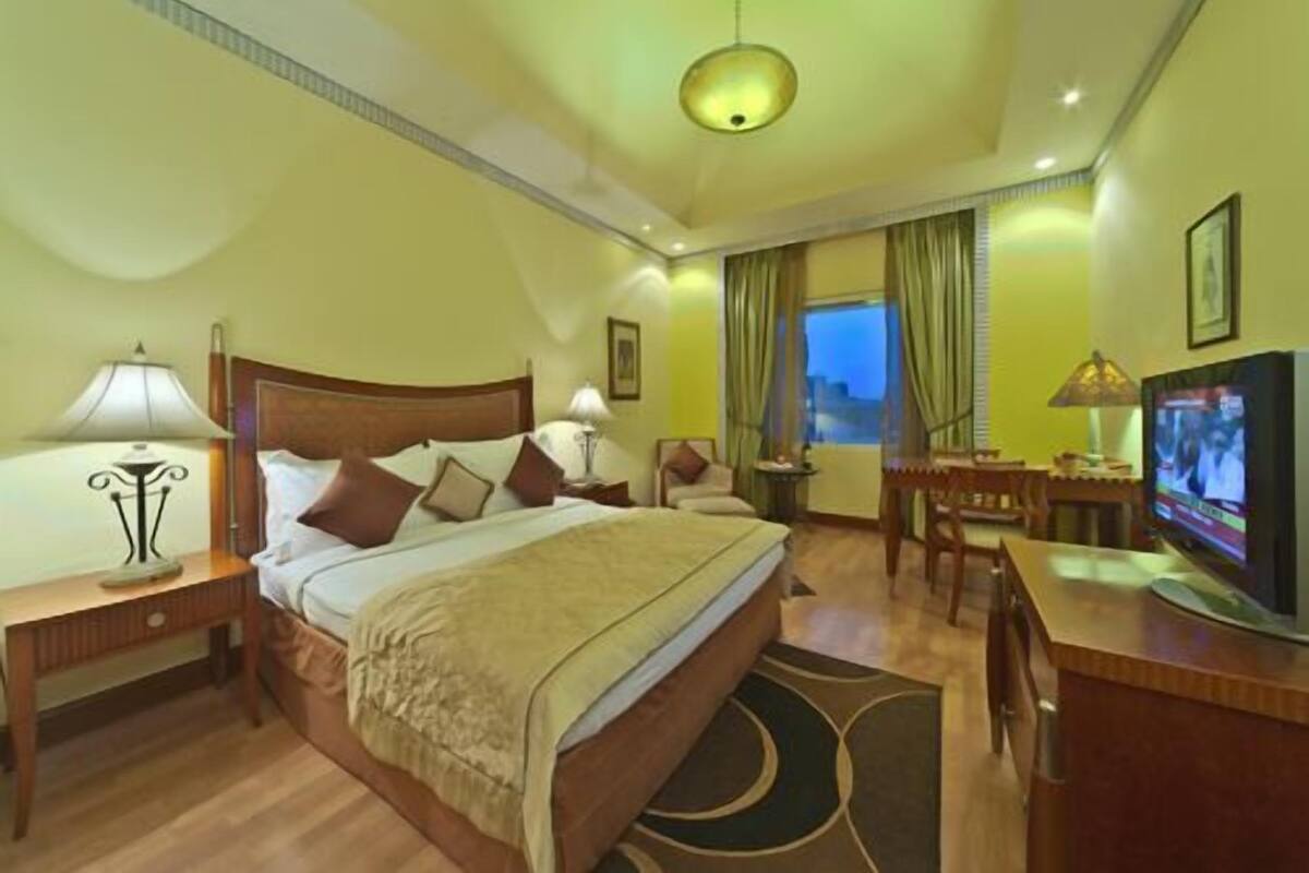 A hotel room with a large bed, bedside tables, a desk with a chair, a television, and a view of the outside.