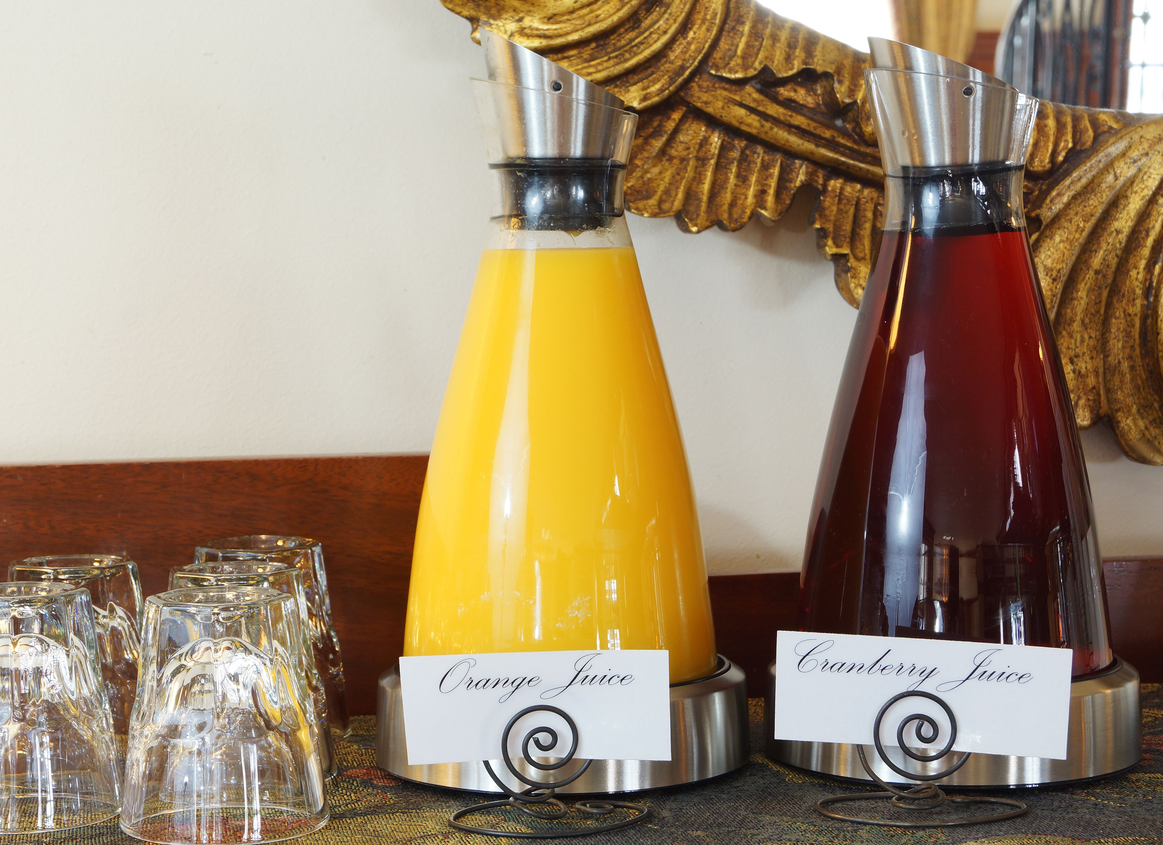 Two juice dispensers labeled "Orange Juice" and "Cranberry Juice" with glasses and a decorative wall in the background.