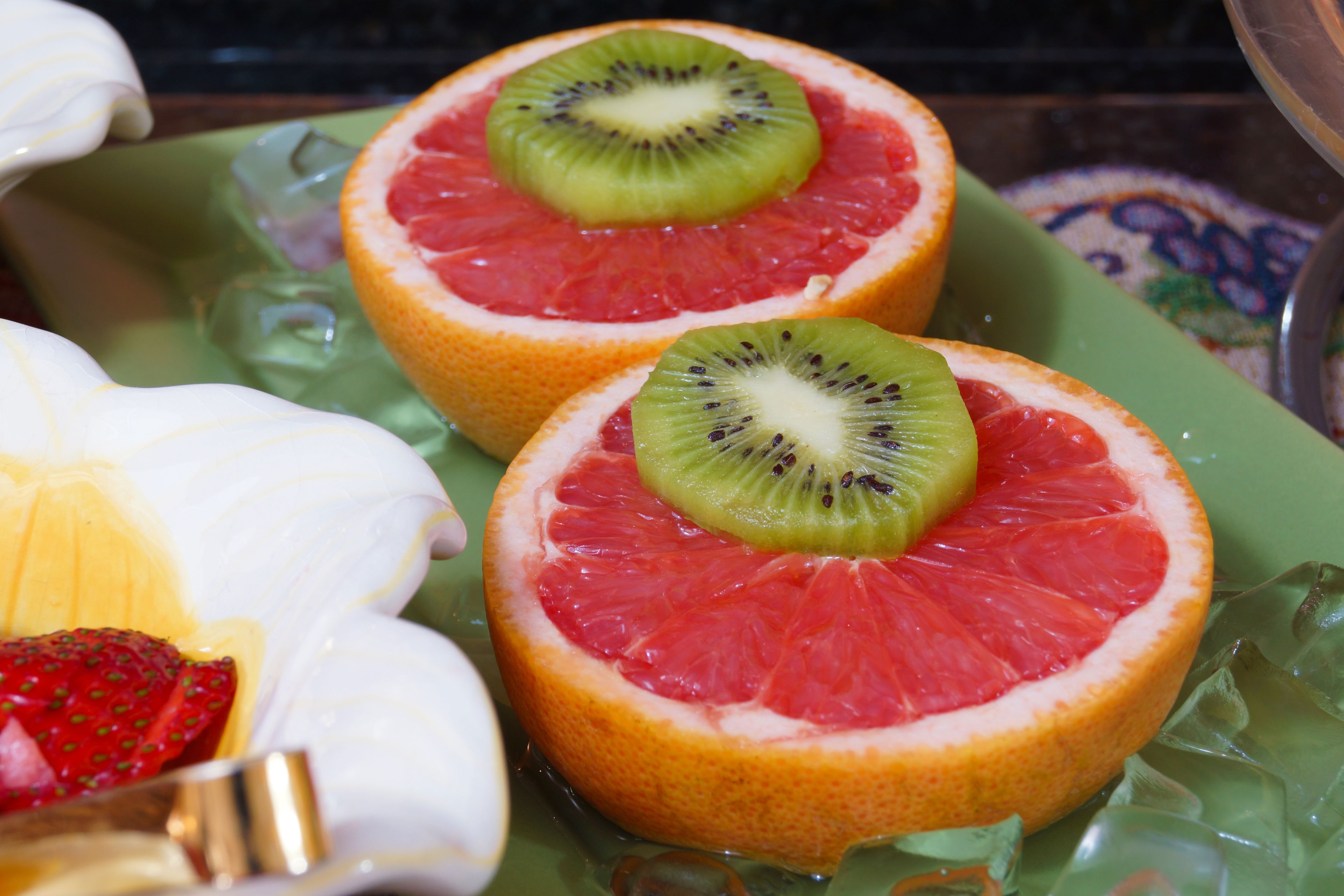 Dos mitades de pomelo con rodajas de kiwi sobre un plato verde.