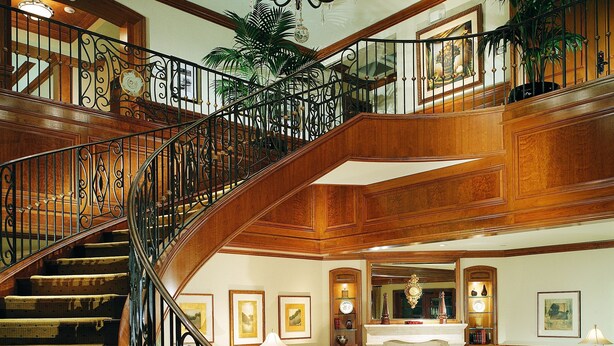 A grand staircase with ornate railings leading to an upper floor, a cozy sitting area with a fireplace, and a chandelier. - The Rose Hotel (Pleasanton)