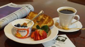 A breakfast setting with a cup of coffee, a bowl of yogurt with fruit, a slice of toast, and a newspaper on a table.
