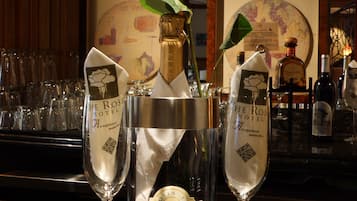 Une bouteille de champagne dans un seau en métal est posée sur le comptoir d’un bar, flanquée de deux coupes à champagne.
