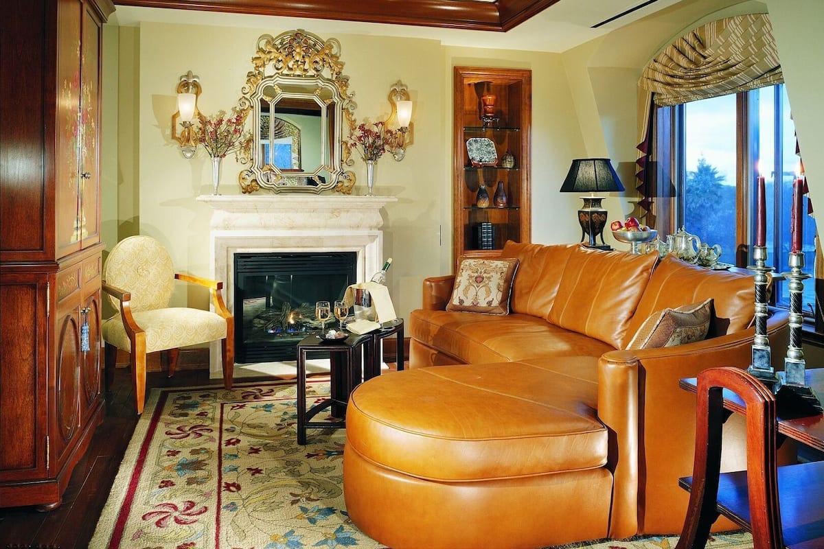 A living room with a fireplace, leather sofa, wooden cabinet, and a large mirror.