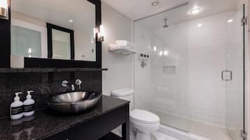A modern bathroom with a large mirror, a vessel sink, a toilet, and a glass-enclosed shower area.