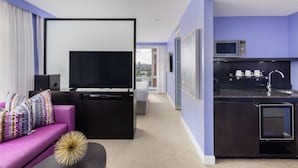 A modern hotel room with a purple sofa, a flat-screen TV, a small kitchen with a microwave, and a city view. - OPUS Hotel Vancouver (Vancouver)