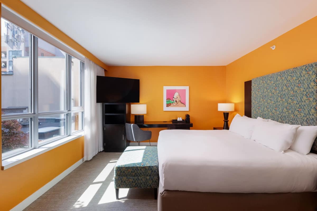 Una habitación de hotel con una cama grande, un escritorio con una silla, un televisor y una ventana con cortinas.