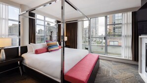 A modern hotel room with a four-poster bed, large windows offering city views, a desk with a lamp, and a red bench. - OPUS Hotel Vancouver (Vancouver)