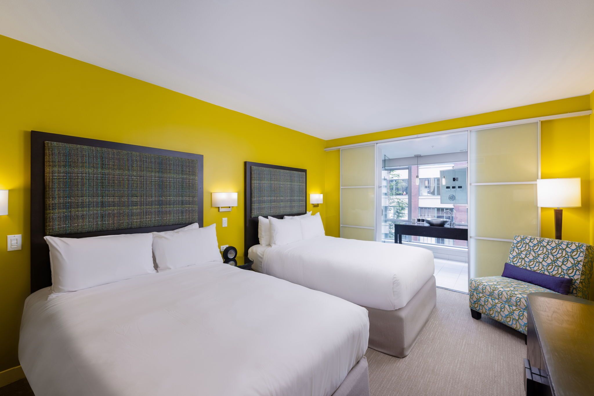 Habitación de hotel con dos camas, una silla y vista al exterior.
