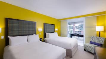 Habitación de hotel con dos camas, una silla y vista al exterior.
