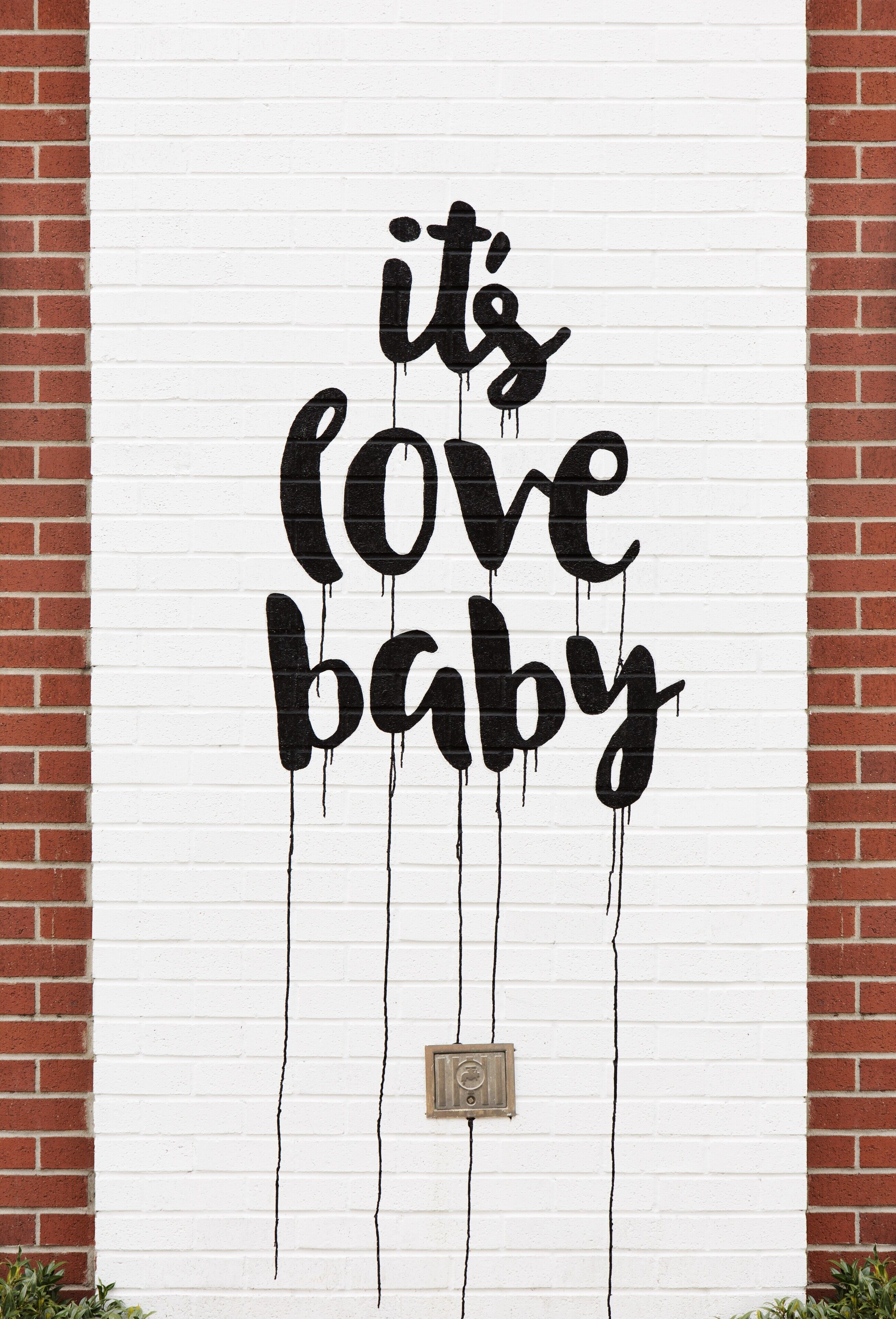 Una pared con la frase 'it's love baby' en estilo graffiti negro.