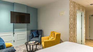 A hotel room with a large bed, a flat-screen TV mounted on the wall, two armchairs, a small table, and a patterned door.