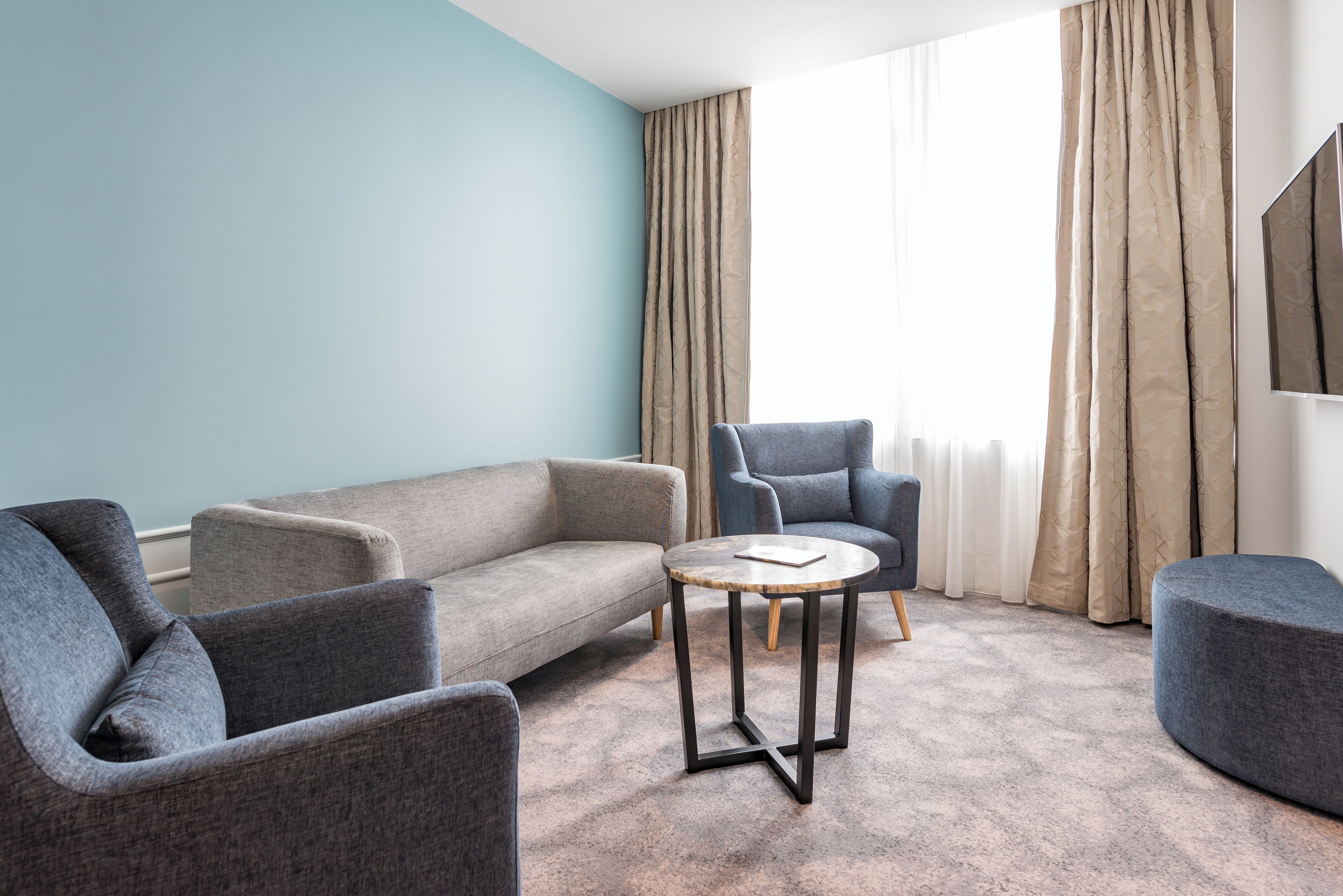 Una sala moderna con un sofá gris, una mesa de centro redonda y un sillón azul.