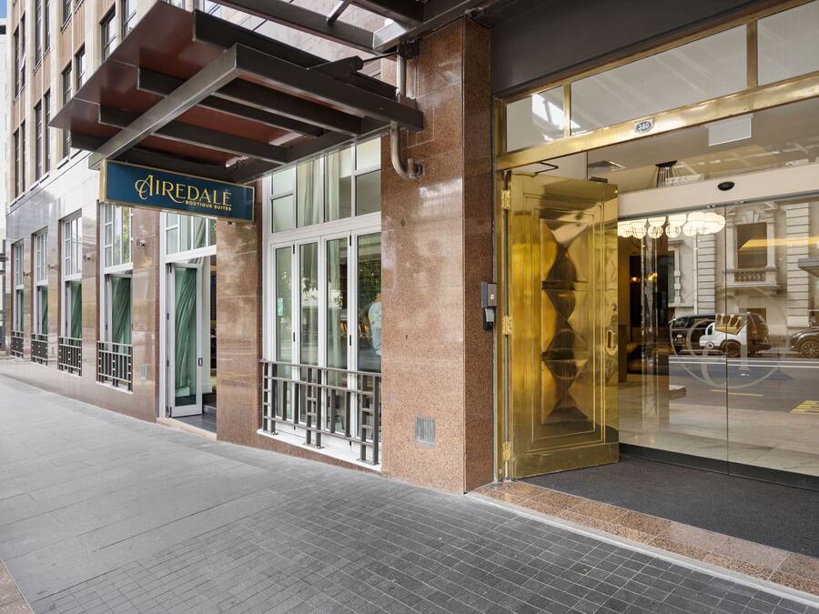 Entrada de hotel com placa indicando 'Airedale Boutique Suites', uma porta de vidro e guarda-corrimão metálico na parte externa.