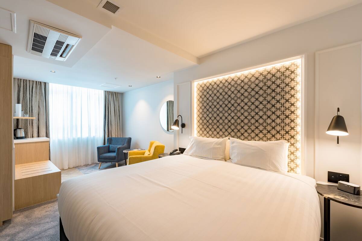 A modern hotel room with a large bed, a desk, a chair, and a vanity with a mirror.