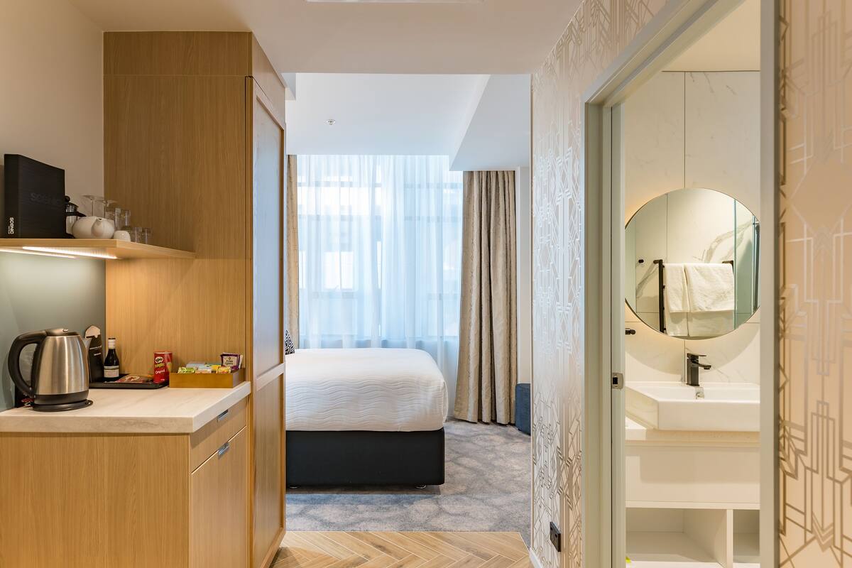 A hotel room with a bed, a desk with a kettle, a coffee maker, and a minibar.
