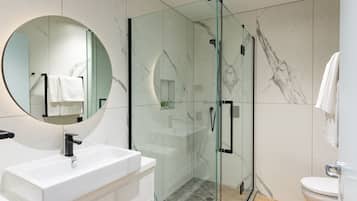 A modern bathroom with a glass-enclosed shower, a white sink, and a round mirror.