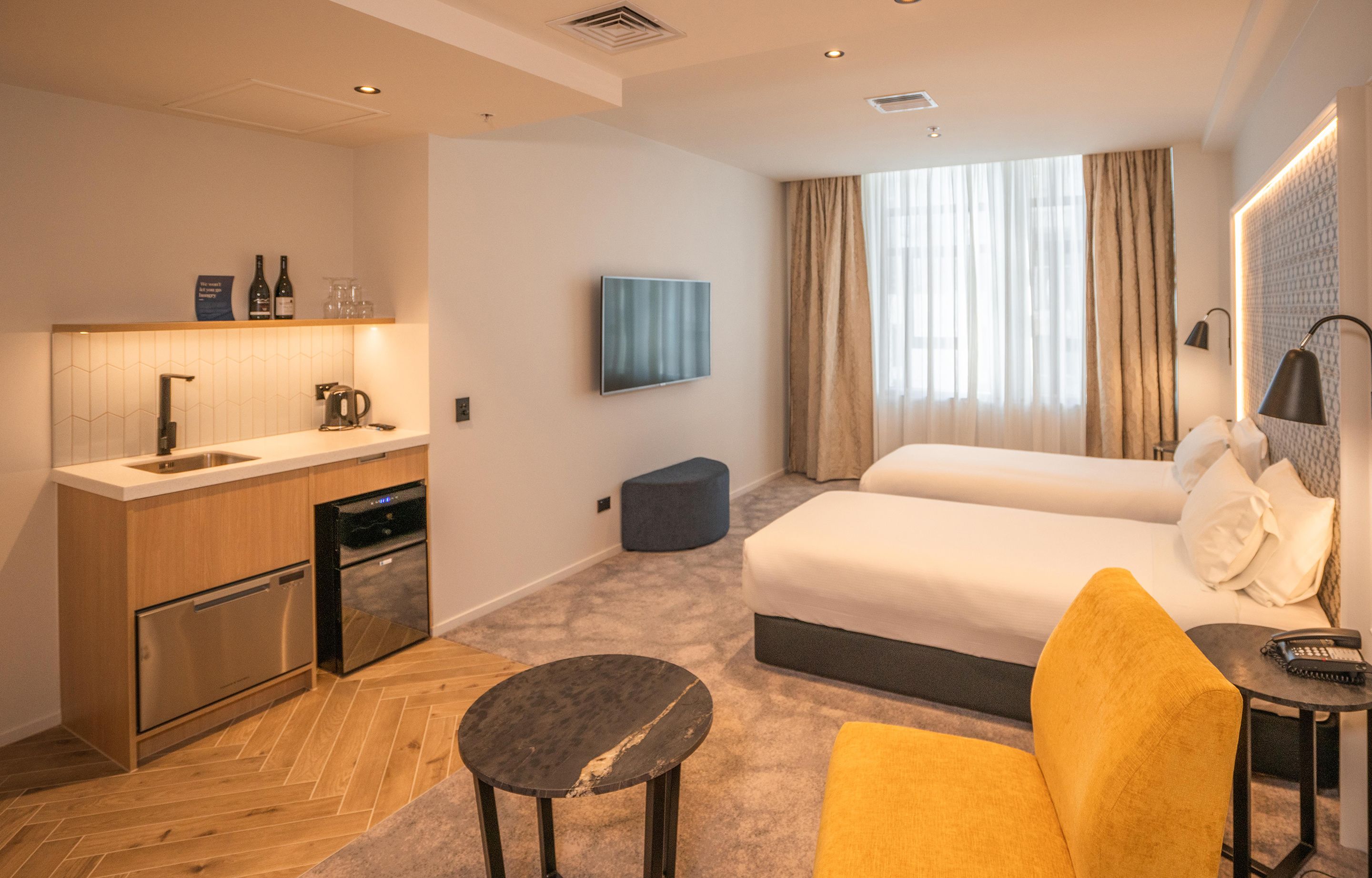 A hotel room with a kitchenette, a bed, a sofa, and a TV.