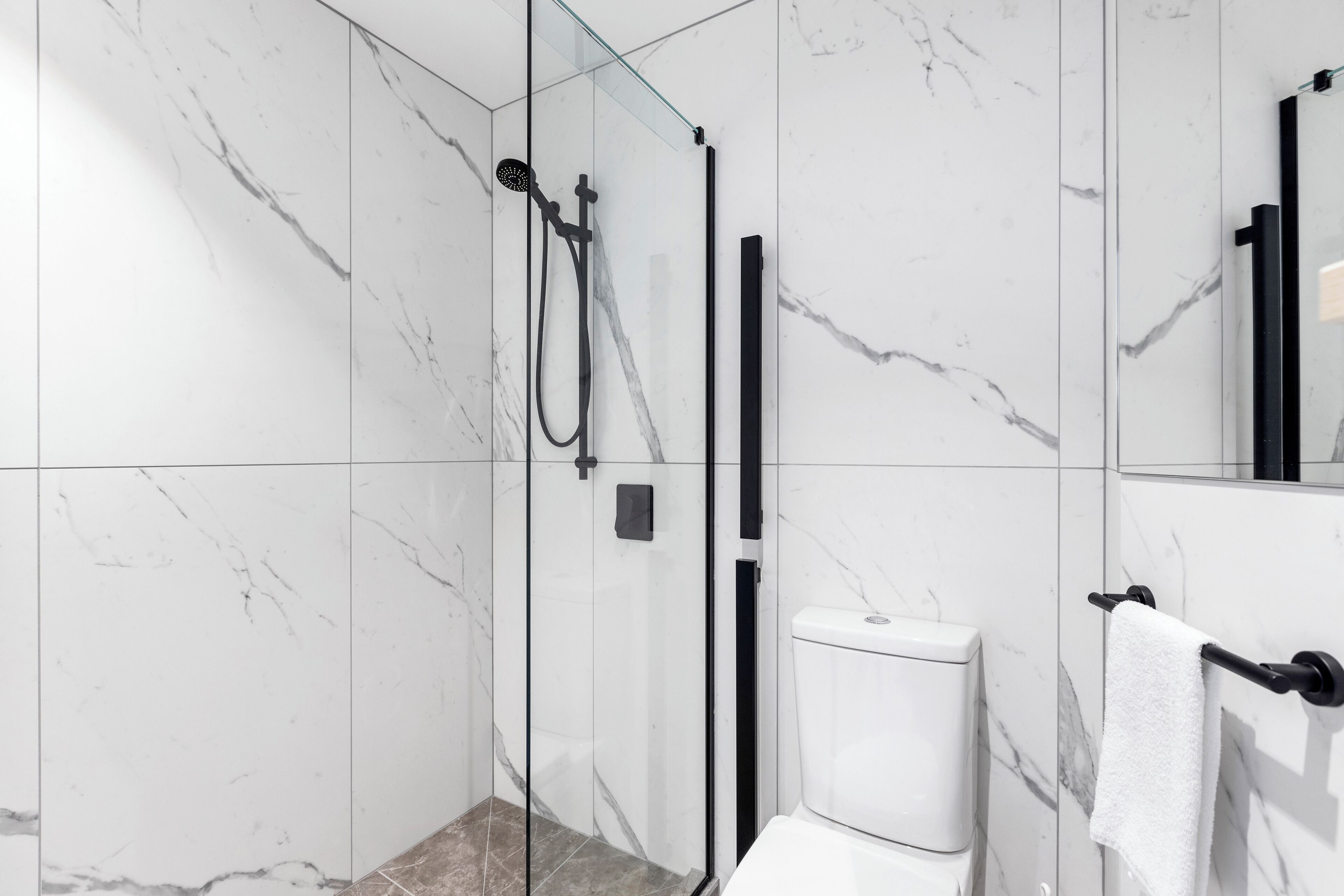A modern bathroom with a glass-enclosed shower, a toilet, and a towel rack.