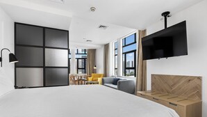 A modern hotel room with a large bed, a flat-screen TV, a wooden headboard, a desk, and a sofa. - Legacy Airedale Hotel Auckland (Auckland)