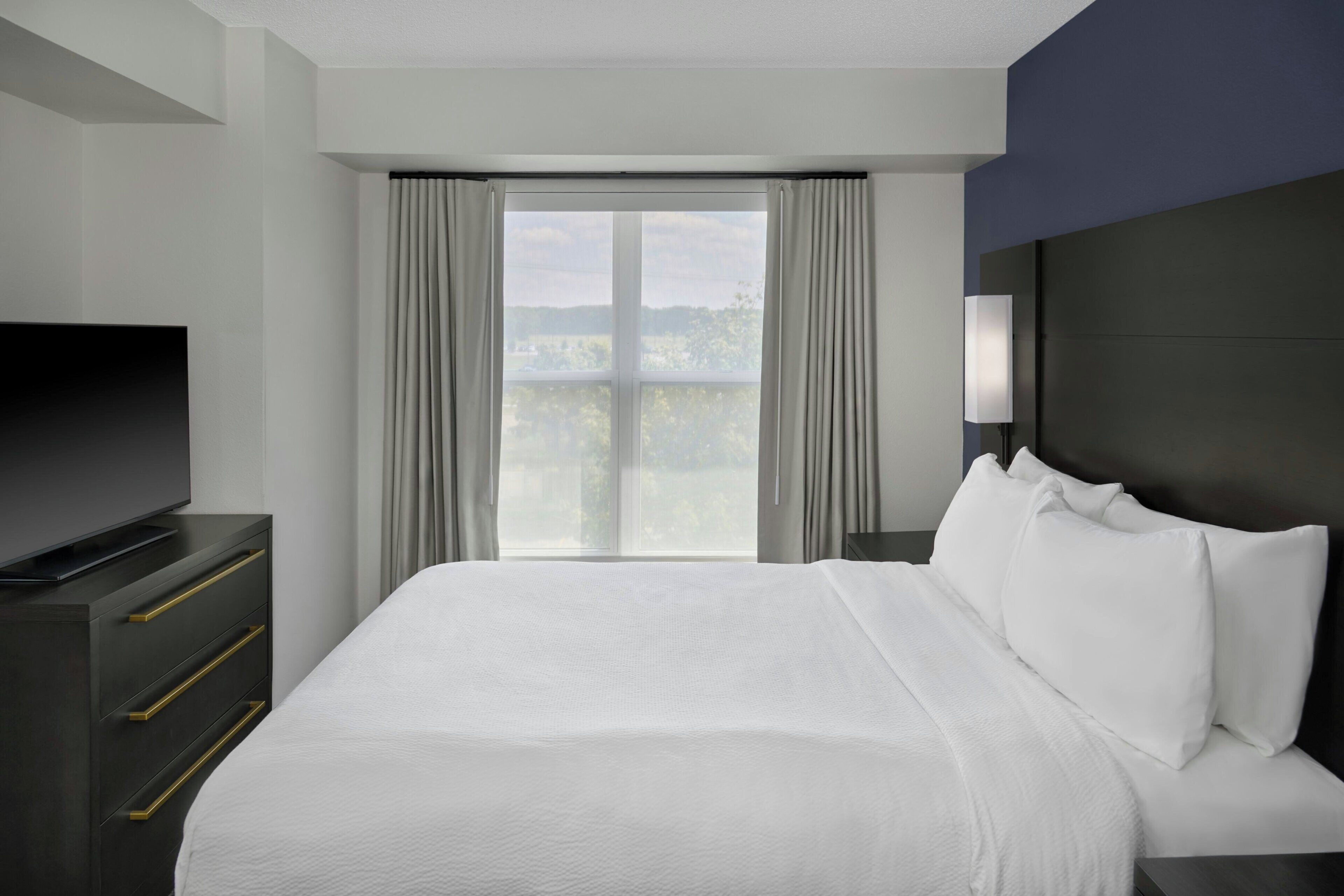 A hotel room with a large bed, a TV on a dresser, a nightstand, and a window with curtains.