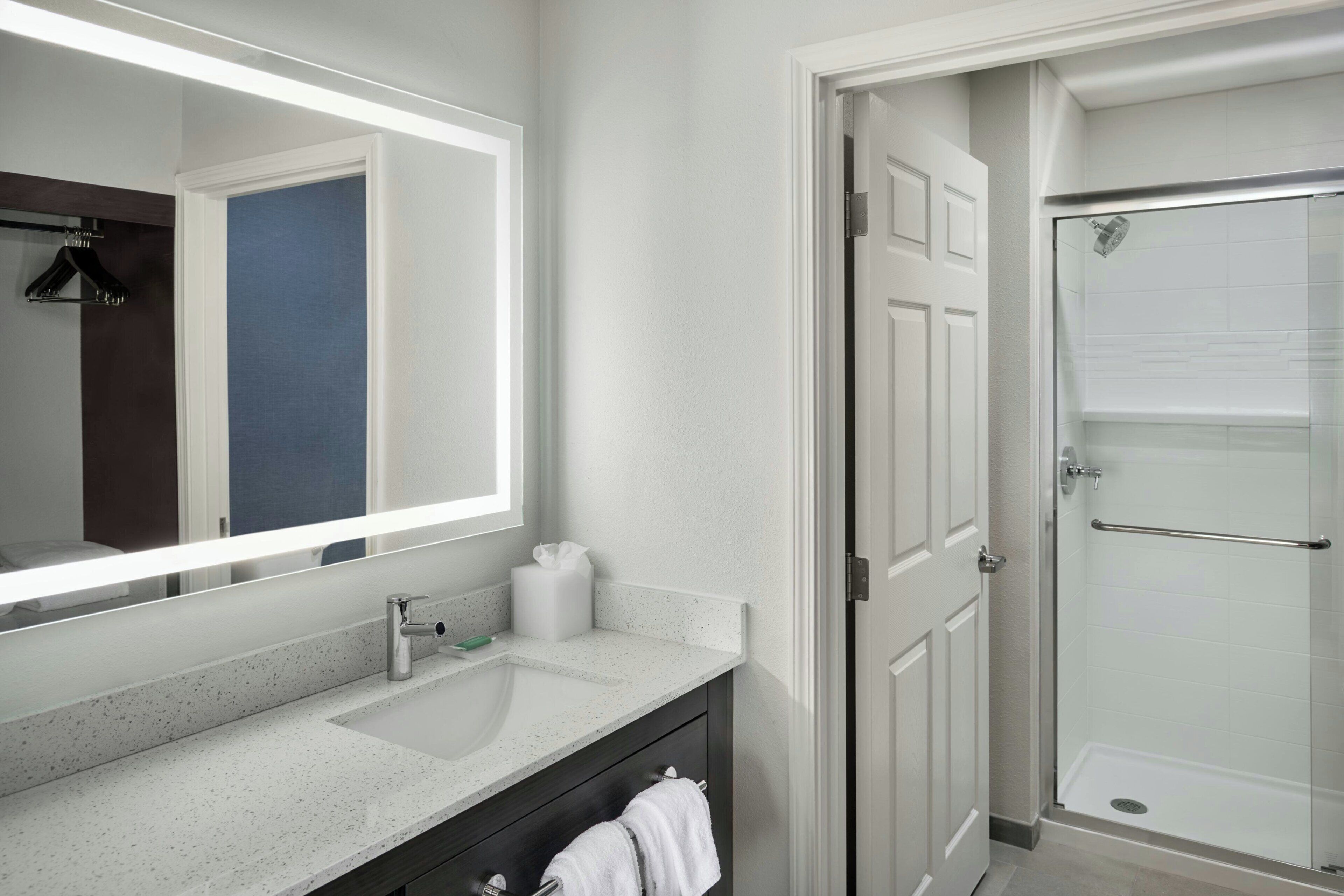 A bathroom with a large mirror, a sink, a towel rack, and a shower area.