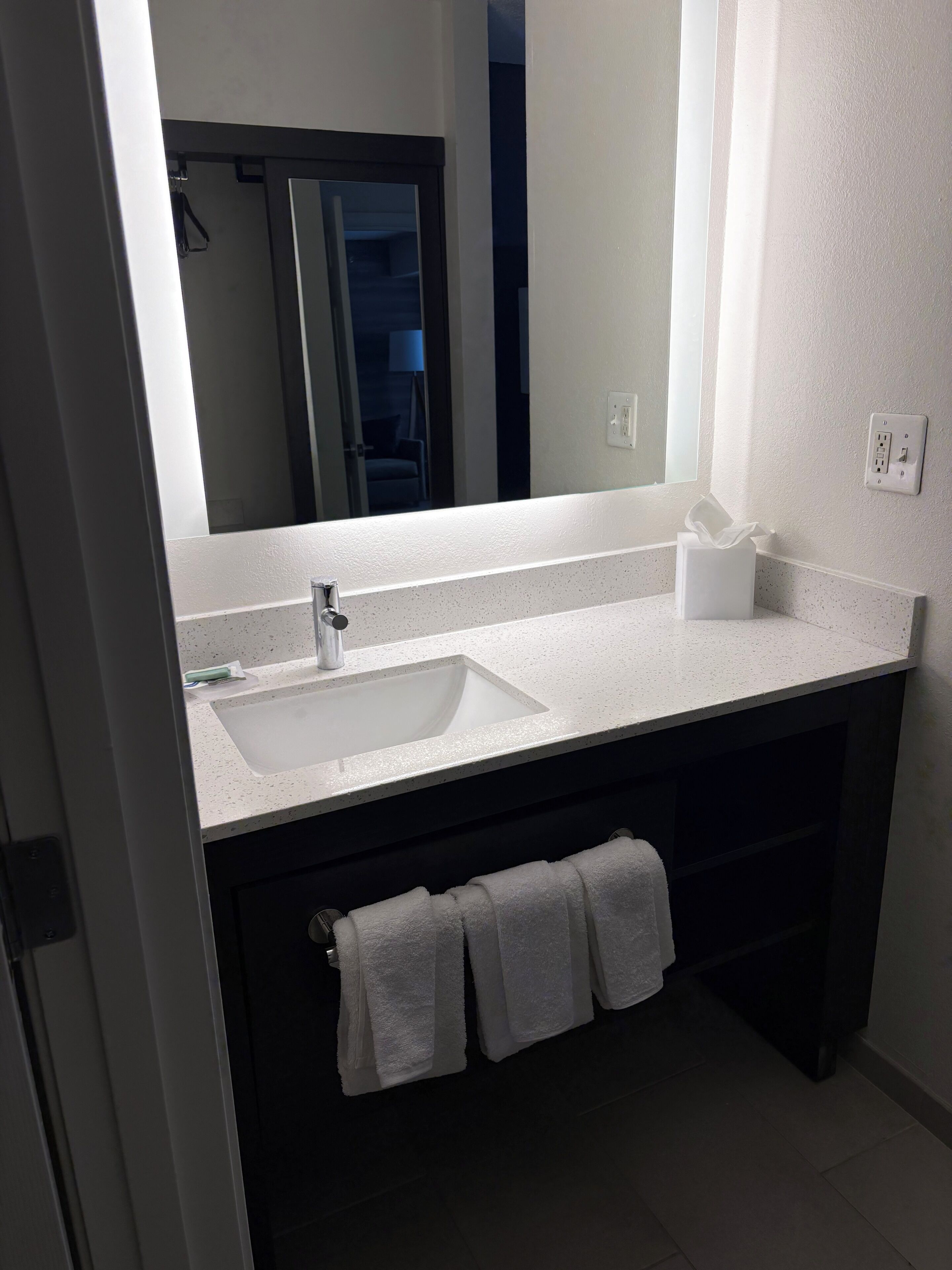 A bathroom with a large mirror, a sink, a towel rack, and a toilet.