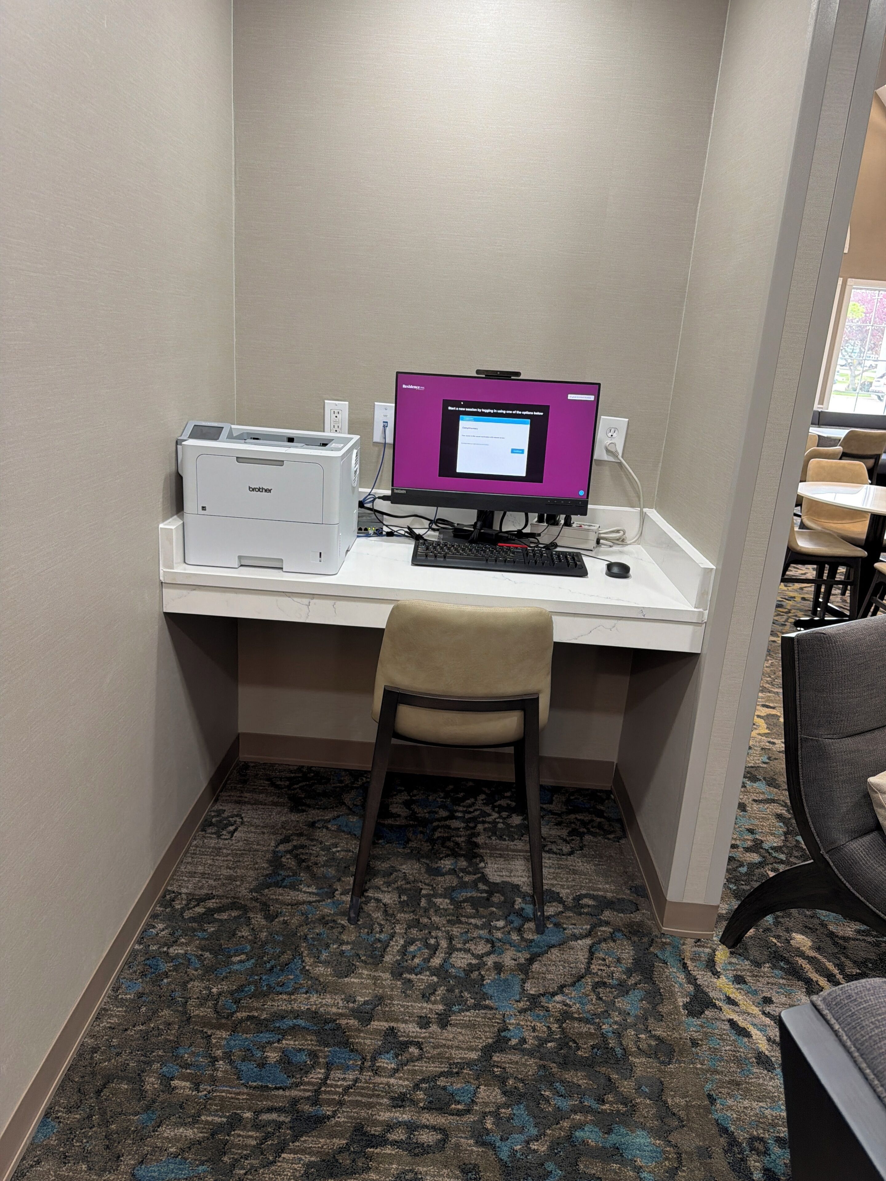 A corner desk with a computer, printer, and chair in a hotel room.