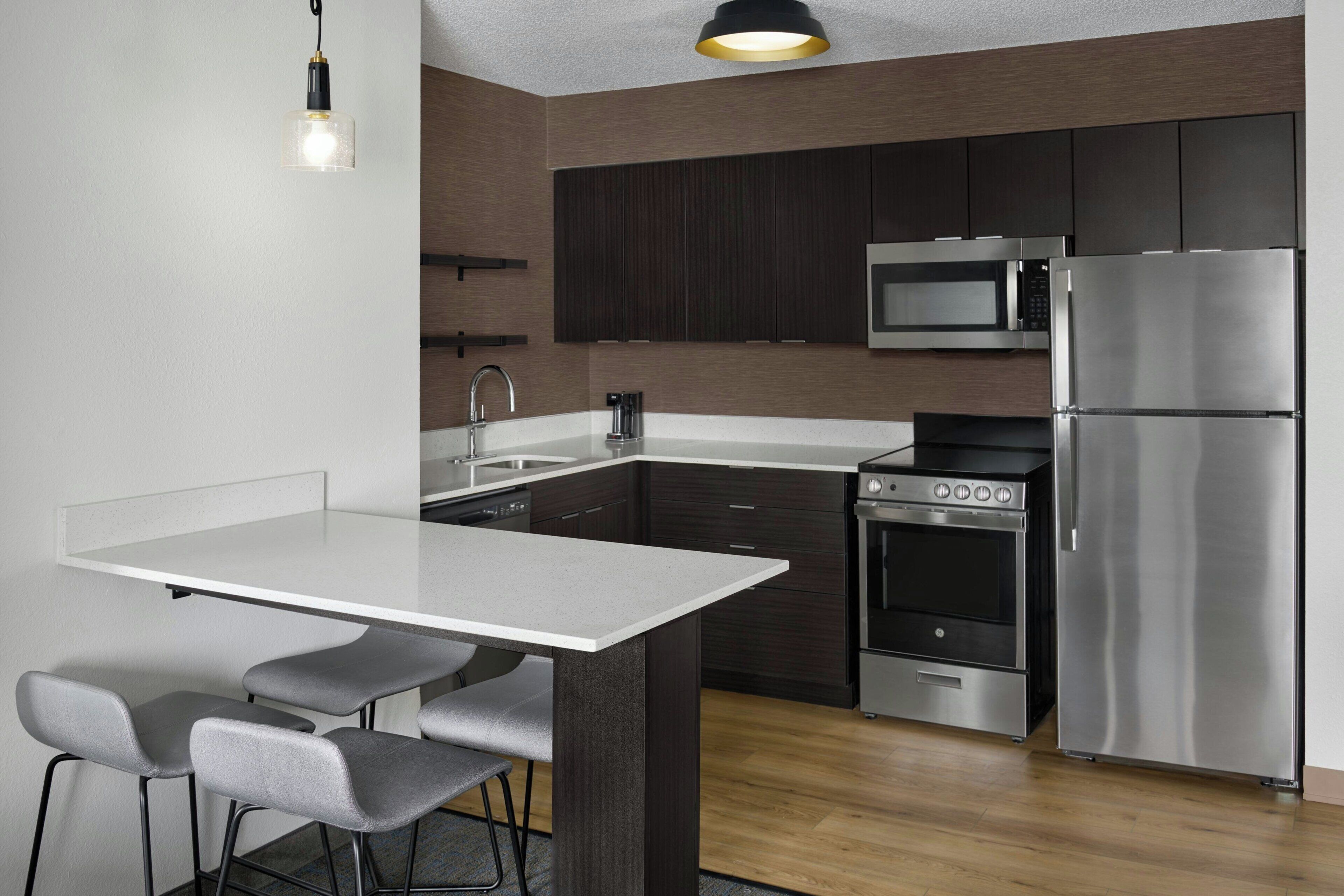 A modern kitchen with a central island, stainless steel appliances, and a bar stool seating arrangement.