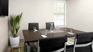 A conference room with a long table, four chairs, a potted plant, and a window.