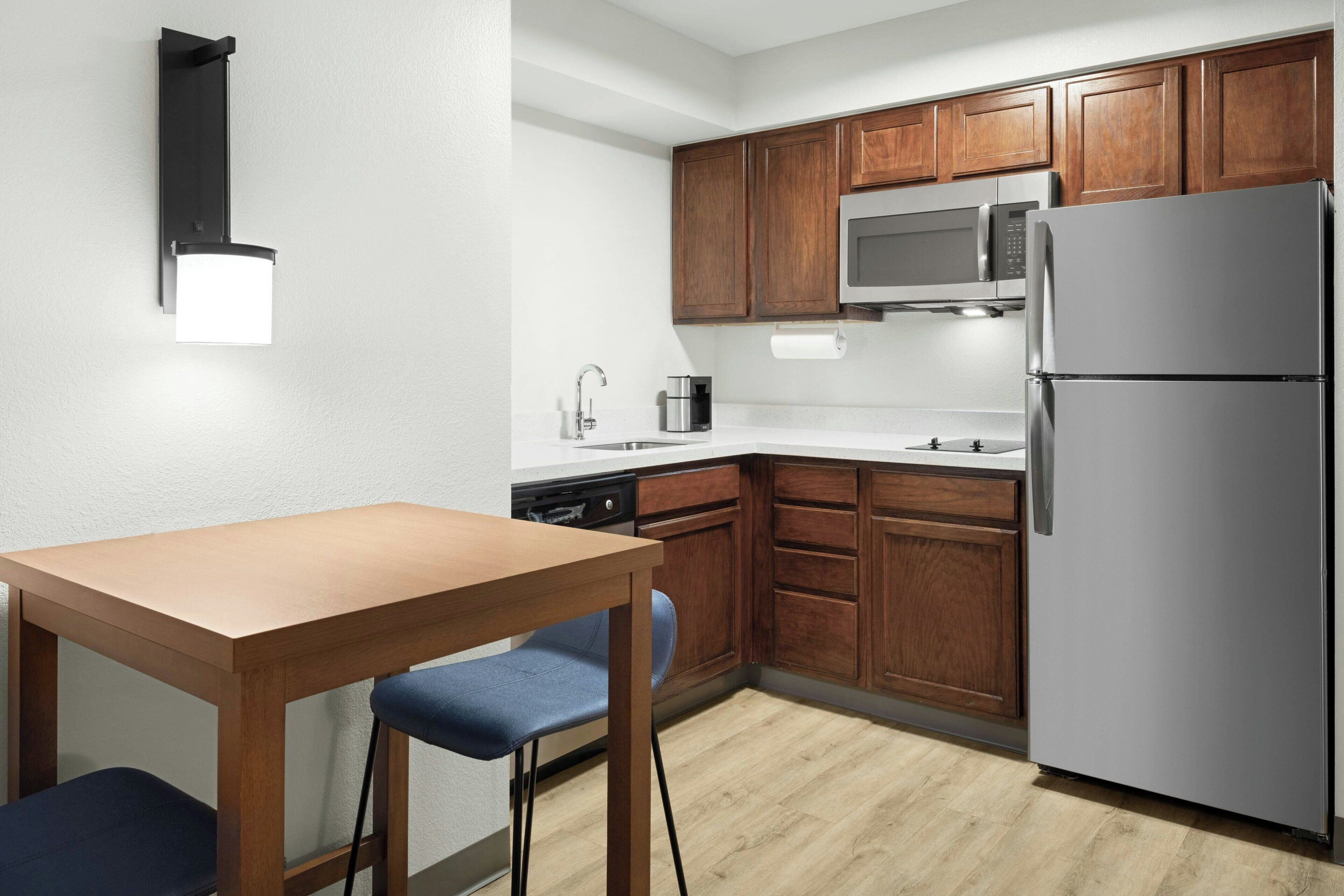 A compact kitchen with wooden cabinets, a stainless steel refrigerator, a microwave, and a sink.