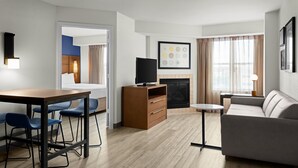 Une chambre d’hôtel moderne avec un plancher en bois, un canapé, une télévision, une cheminée et un coin repas avec des chaises.