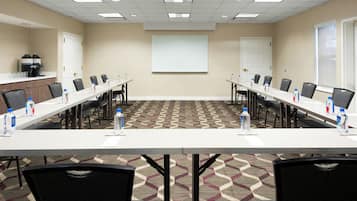 A conference room with a long table, chairs, a projector screen, and a coffee machine.