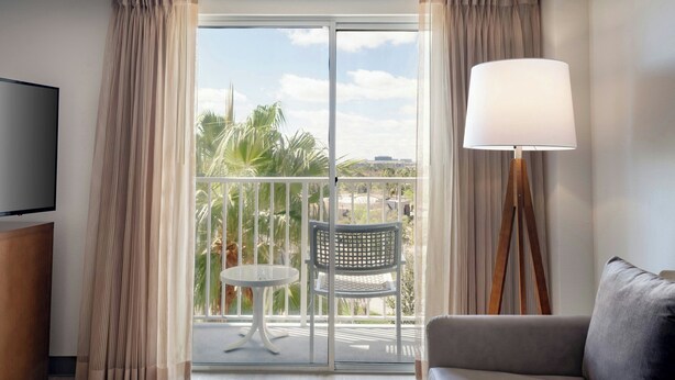 Une chambre d’hôtel avec un balcon, un canapé, une table avec deux chaises, une lampe et un téléviseur.
